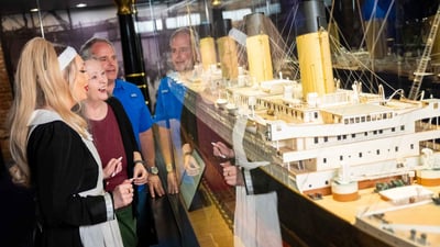 An image of a couple standing at a Titanic model with a crew member learning about the famous ship. 