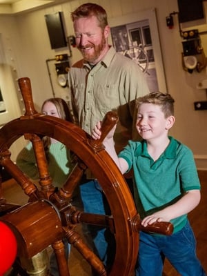 A young boy and his father stand at the ship's wheel at the Titanic Museum Attraction.