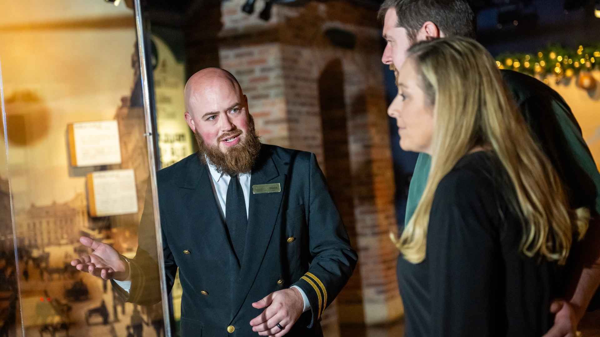 Titanic crew member at artifact case with guests, giving information.